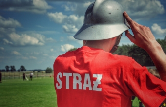 Strazak w czerwonej koszulce z napisem straz i szarym helmie
