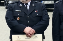 Mężczyzna w mundurze strażackim trzymający w rękach dokument o dofinansowaniu 